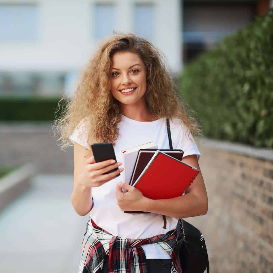 Estudante distraída segurando livros e celular, focada na busca por informações sobre o IFES.