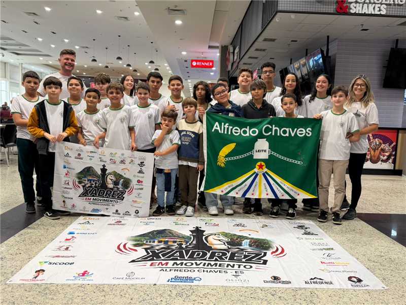Competição de xadrez em Aracruz com alunos de Alfredo Chaves segurando a bandeira do município.