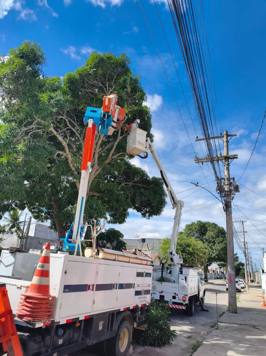 Fotografia de técnicos eletricistas da distribuidora de energia EDP trabalhando com equipamentos de segurança em um cesto aéreo elevado, realizando a poda de galhos de árvores próximos aos fios de alta tensão no Centro da cidade, ilustrando o mutirão da EDP em Montanha em matéria do portal Informe Capixaba.