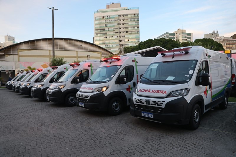 Fileira de ambulâncias brancas com logomarca do Governo do Espírito Santo estacionadas durante evento de entrega.