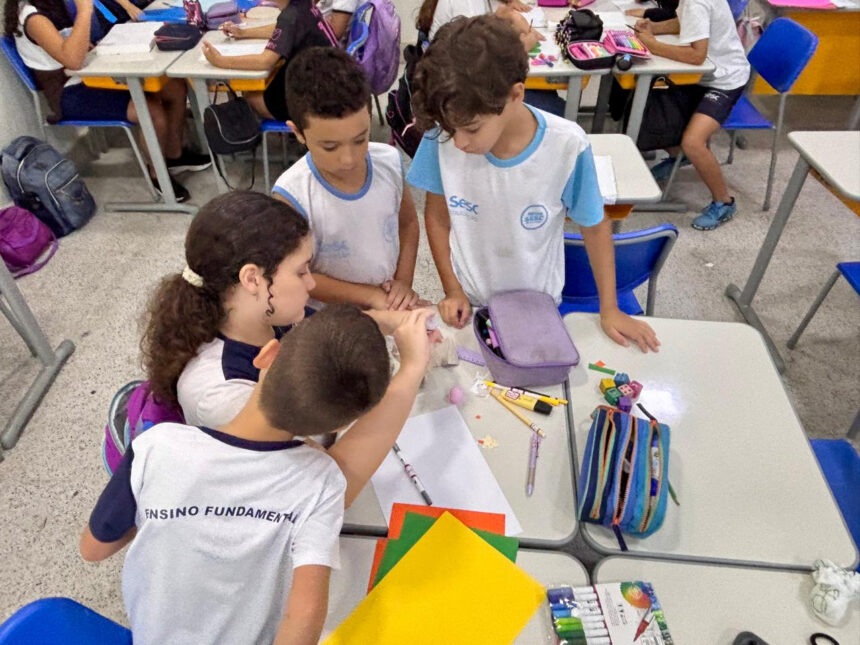 Crianças concentradas realizando uma atividade científica com garrafas e maquetes coloridas em sala de aula do Sesc.