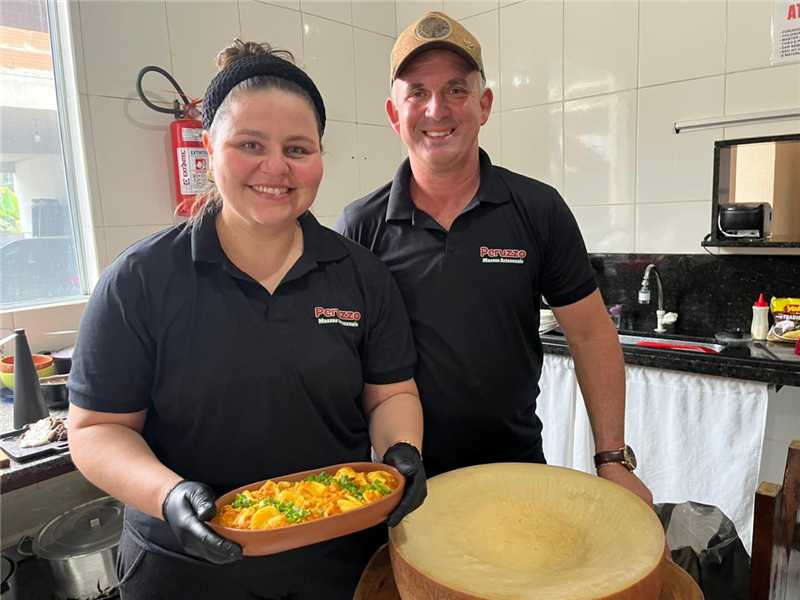 Chefe de cozinha misturando macarrão quente dentro de uma enorme peça de queijo Grana Padano no Festival de Inverno de Matilde.
