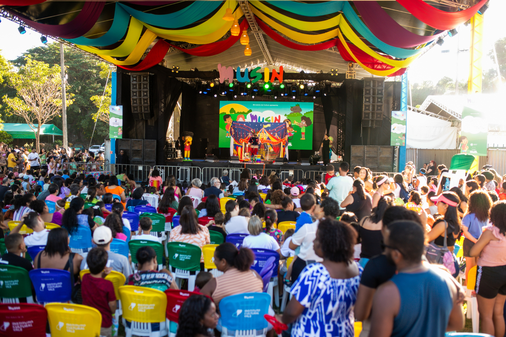 Crianças e pais assistindo a um espetáculo musical ao ar livre durante o festival infantil gratuito em Vitória.