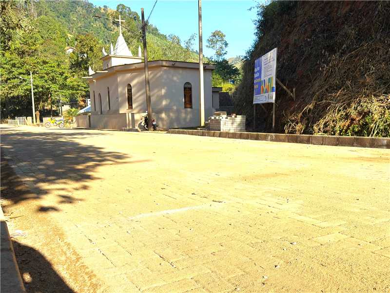 Trator e operários realizando serviços de infraestrutura e pavimentação em estrada de terra.