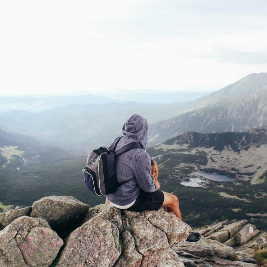 Homem sentado sobre uma pedra no topo de um monte olhando o horizonte aberto, representando a força da naturalidade e a conexão com a essência divina.