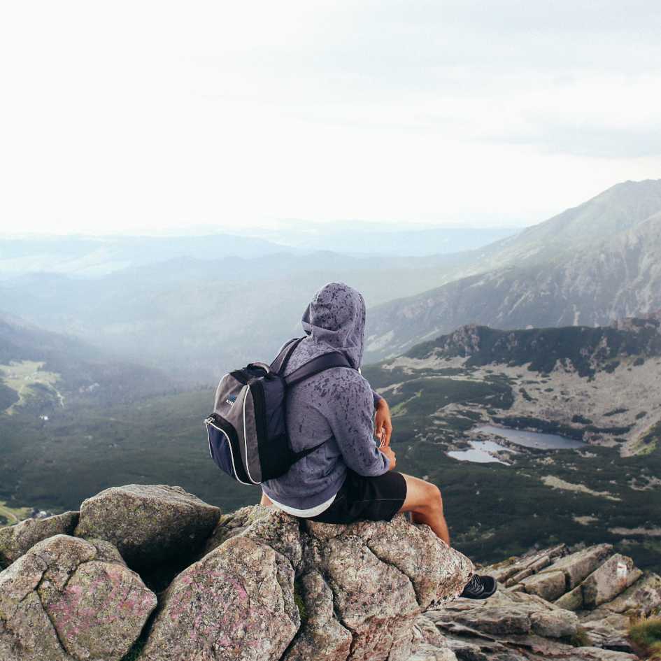 Homem sentado sobre uma pedra no topo de um monte olhando o horizonte aberto, representando a força da naturalidade e a conexão com a essência divina.