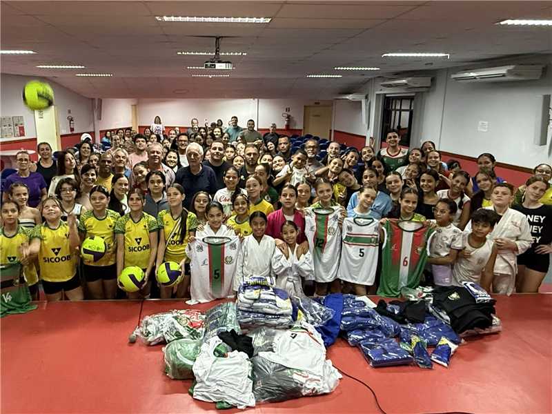 Autoridades municipais posam ao lado de caixas e pacotes com kimonos, tatames e uniformes esportivos novos no auditório da Secretaria de Educação.