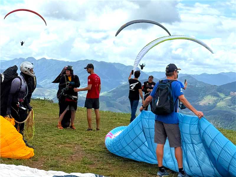 Praticantes de voo livre com parapentes coloridos sobrevoando montanhas verdes na vila de Cachoeira Alta.