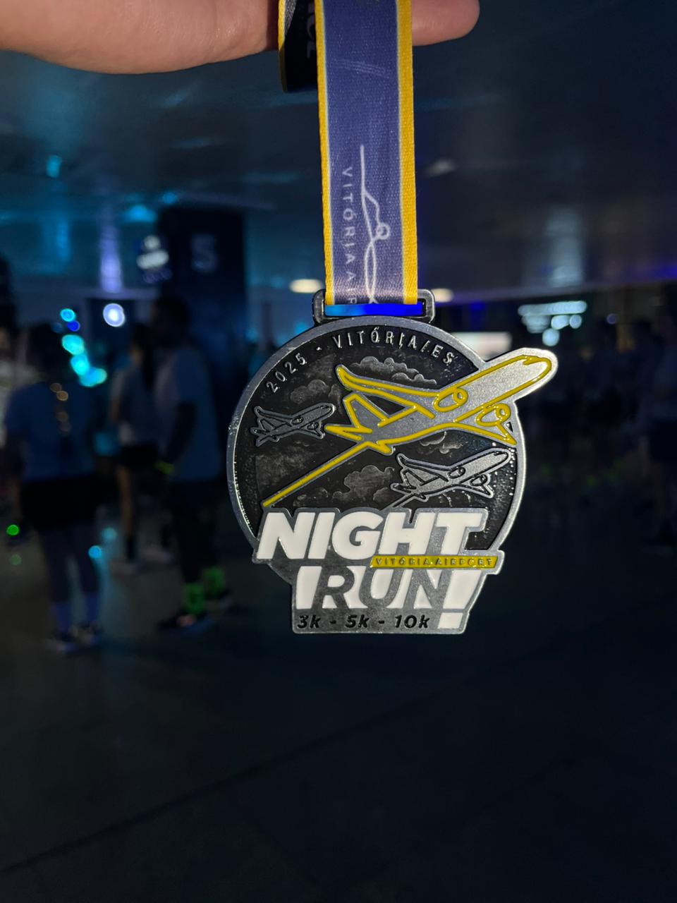 Medalha oficial da Night Run Vitória Airport mantida em destaque com fundo desfocado.